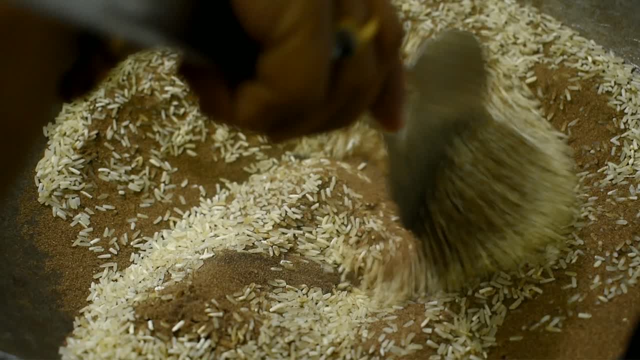 튀김을 위해 뜨거운 모래에 밥을 넣고 밥이 튀길 때까지 저어주는 여자