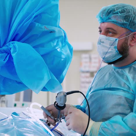 professional doctor conducts kidneys operation. surgeon in blue medical mask and uniform uses modern medical appliance for crushing stones in kidneys.