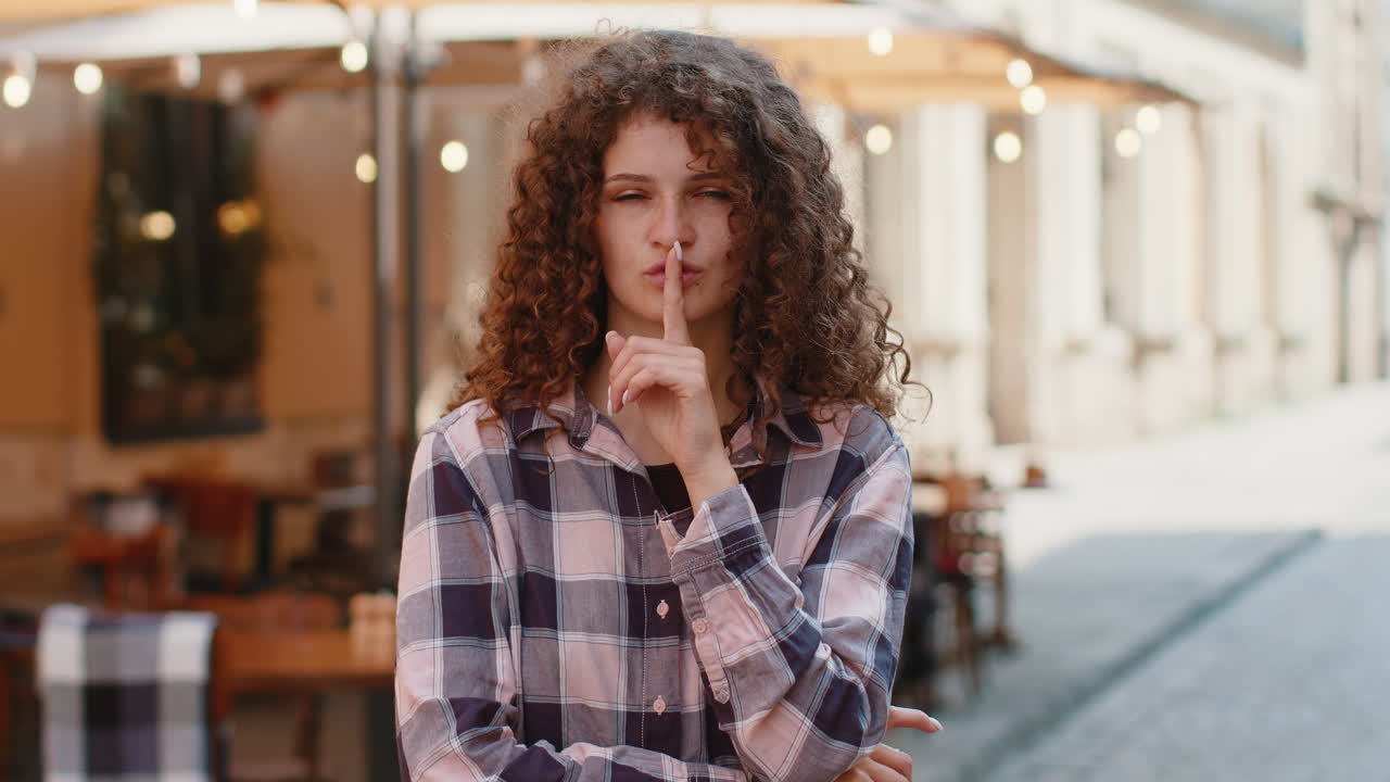 Young woman presses finger to lips makes silence hush sign do not tells gossip secret quiet in city