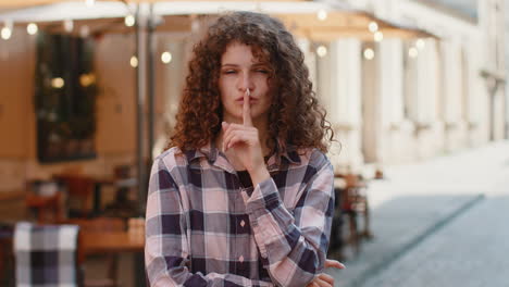young woman presses finger to lips makes silence hush sign do not tells gossip secret quiet in city