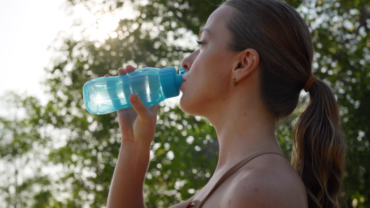 Giovane donna che beve acqua da una bottiglia all'aperto