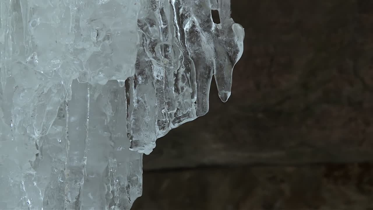 Crystal clear icicle hangs from a frozen cluster inside the Eben Ice Caves in Michigan, with water droplets forming at the tip
