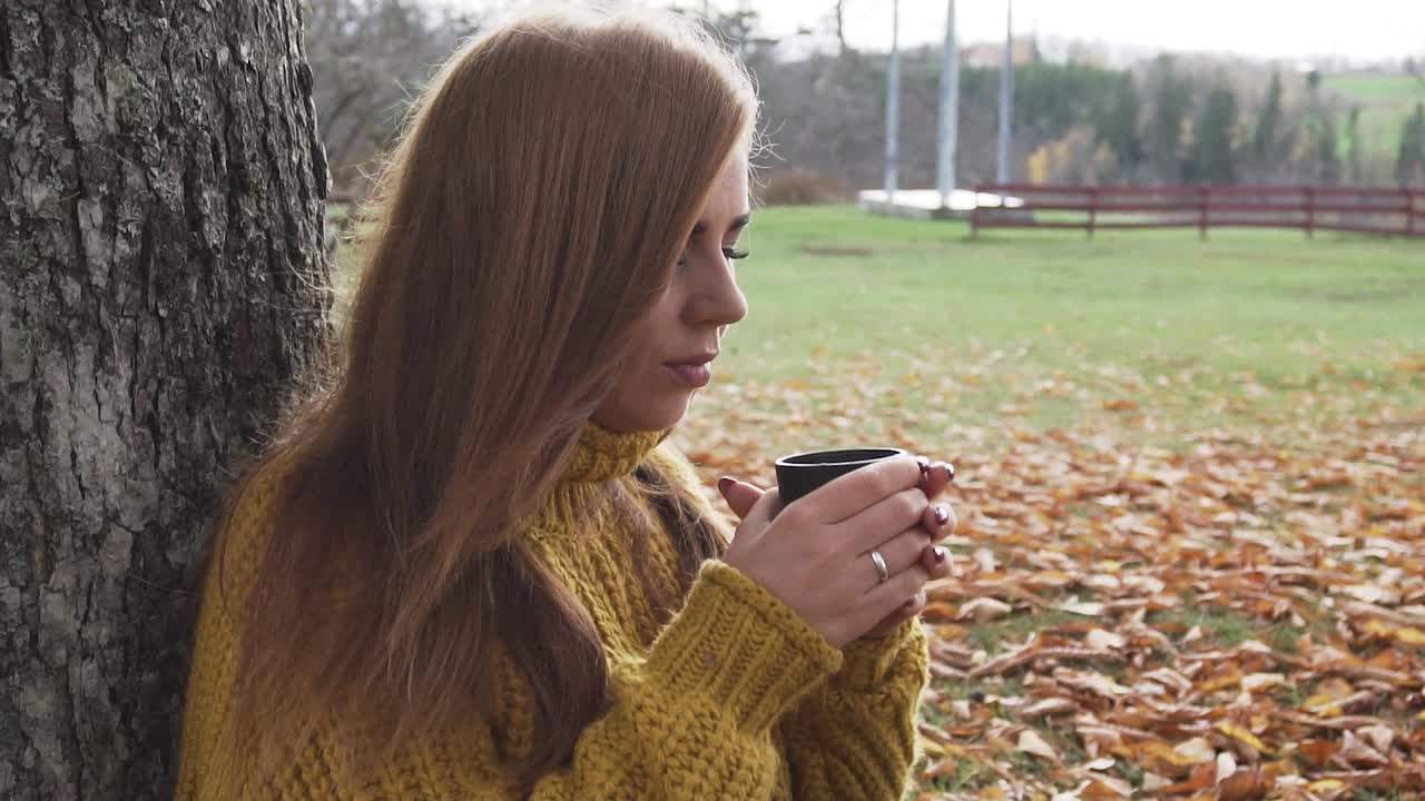 Adult girl is drinking hot beverage at chilly autumn day in slow motion