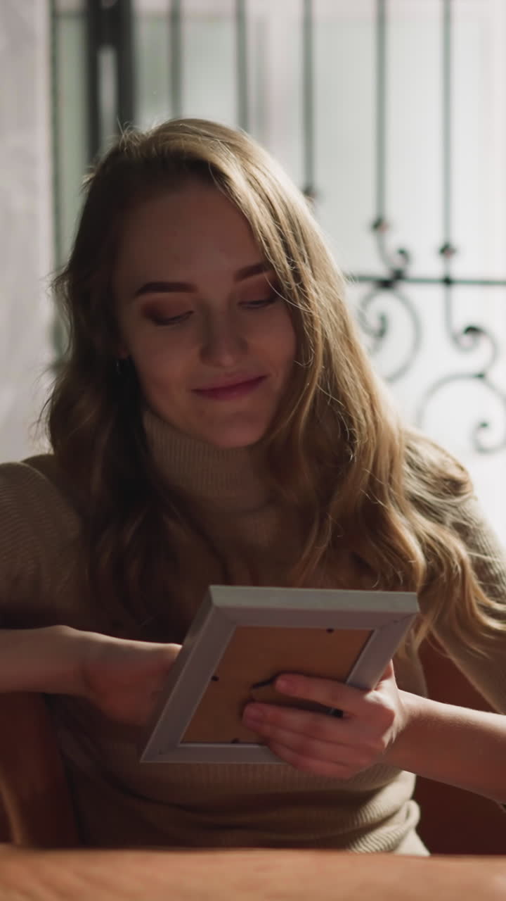 Attractive long haired lady strokes beloved boyfriend picture in frame sitting on comfortable sofa in light living room slow motion