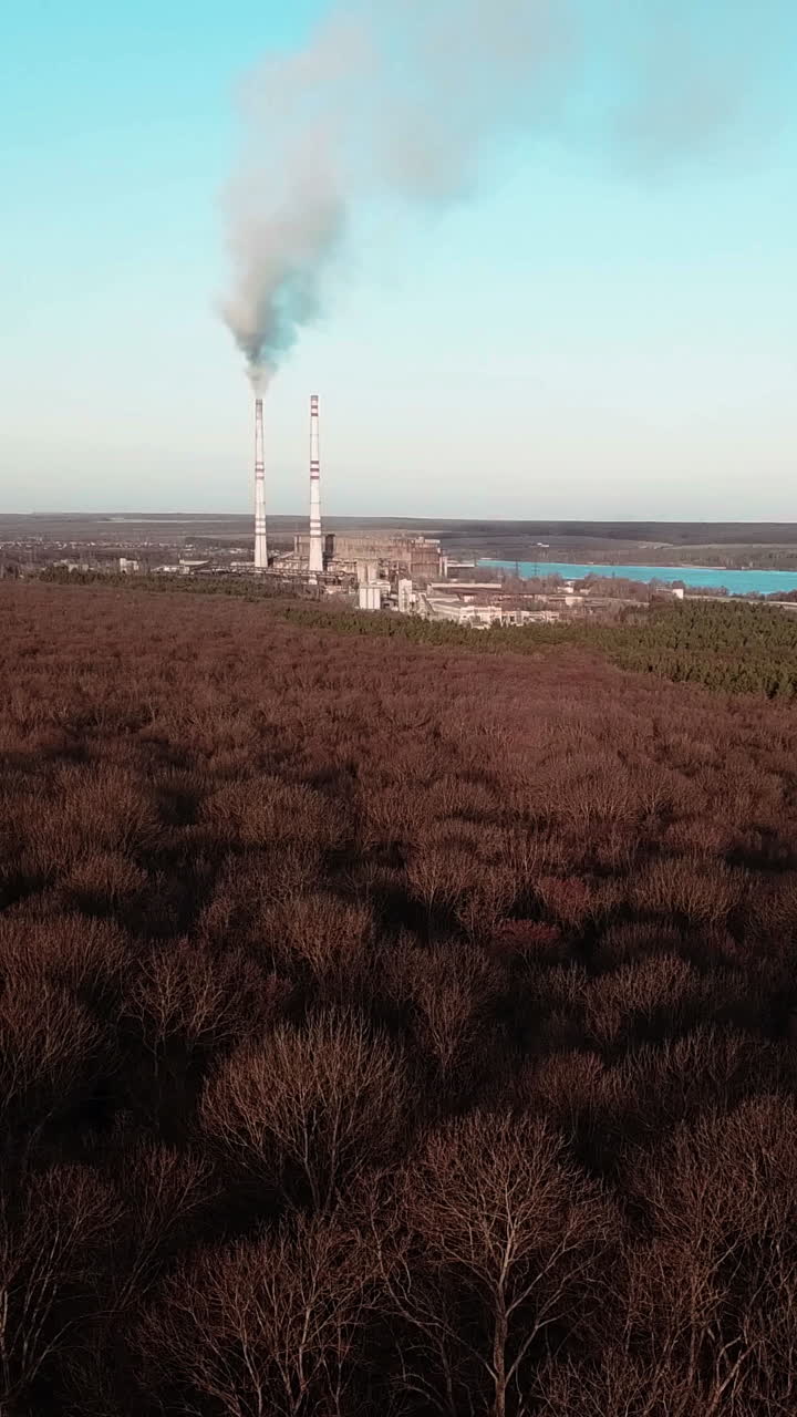 power plant is operating near the forest and the river in the autumn. Aerial view Vertical video