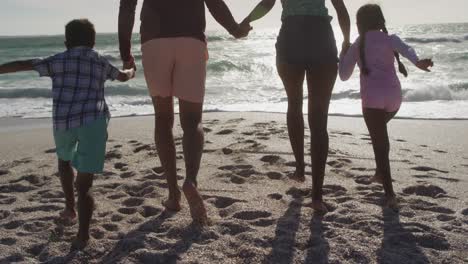 back view of hispanic mother, father, son and daughter holding hands and walking on beach