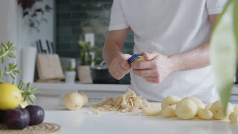 medium shot of a man peeling fresh potatoes with a peeler in a modern kitchen