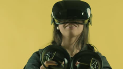 mujer joven jugando con controladores y se pregunta cómo increíble en el auricular vr. casco de realidad virtual en el fondo amarillo. retrato