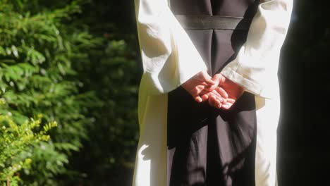 close up shot of the hands of a monk walking in the forest towards the light