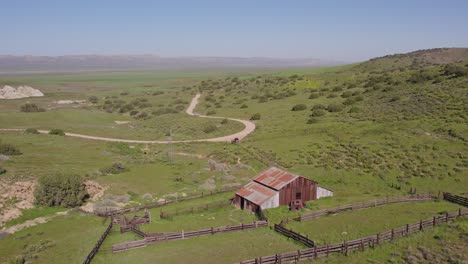 vista aérea soleada de un granero abandonado en las colinas verdes de la llanura de carrizo en california