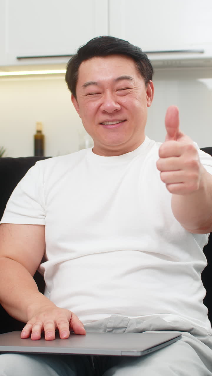 Asian man closes laptop after tasks smiles with pride gives thumbs up then looks at camera calm big