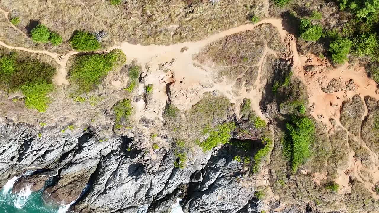 Drone footage capturing rugged cliffs, greenery, and a winding path along the coastline.