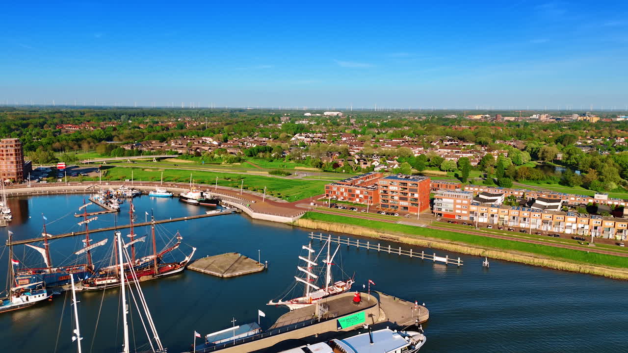 Flying above the boats with sails down standing at the docks. Stunning scenery of Lelystad, the Netherlands in the lush greenery at backdrop.
