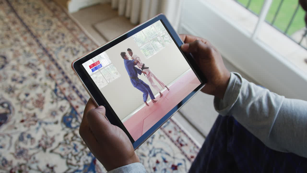 compuesto de un hombre sentado en casa, viendo un partido de judo en la tableta