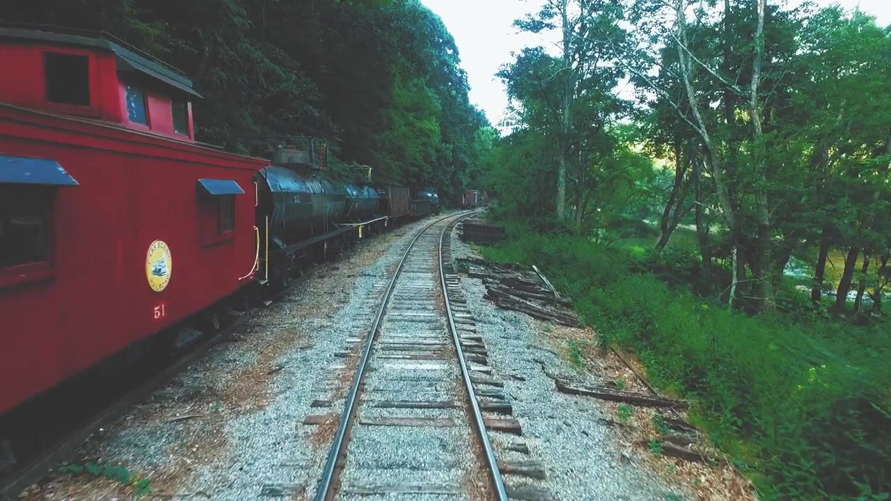 Drone, aereo, bassa quota, carrellata in avanti accanto a vecchie locomotive a vapore Shay e vagoni abbandonati a Cass, Virginia Occidentale. Il fiume Greenbrier è visibile lungo il lato destro dell'inquadratura