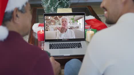 Padre-Birracial-Sonriente-Con-Hijo-Usando-Una-Computadora-Portátil-Para-Una-Videollamada-Navideña-Con-Una-Mujer-Mayor-En-La-Pantalla