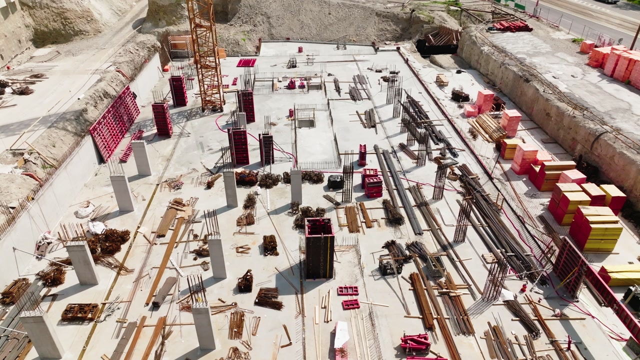 Aerial view of construction site with concrete foundation, columns and building materials. Industrial development process with cranes and structure base in progress, urban infrastructure scene.