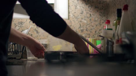a man grabs a hot warm pan and adds water releasing smoke while pouring at the kitchen at home at night medium shot slow motion