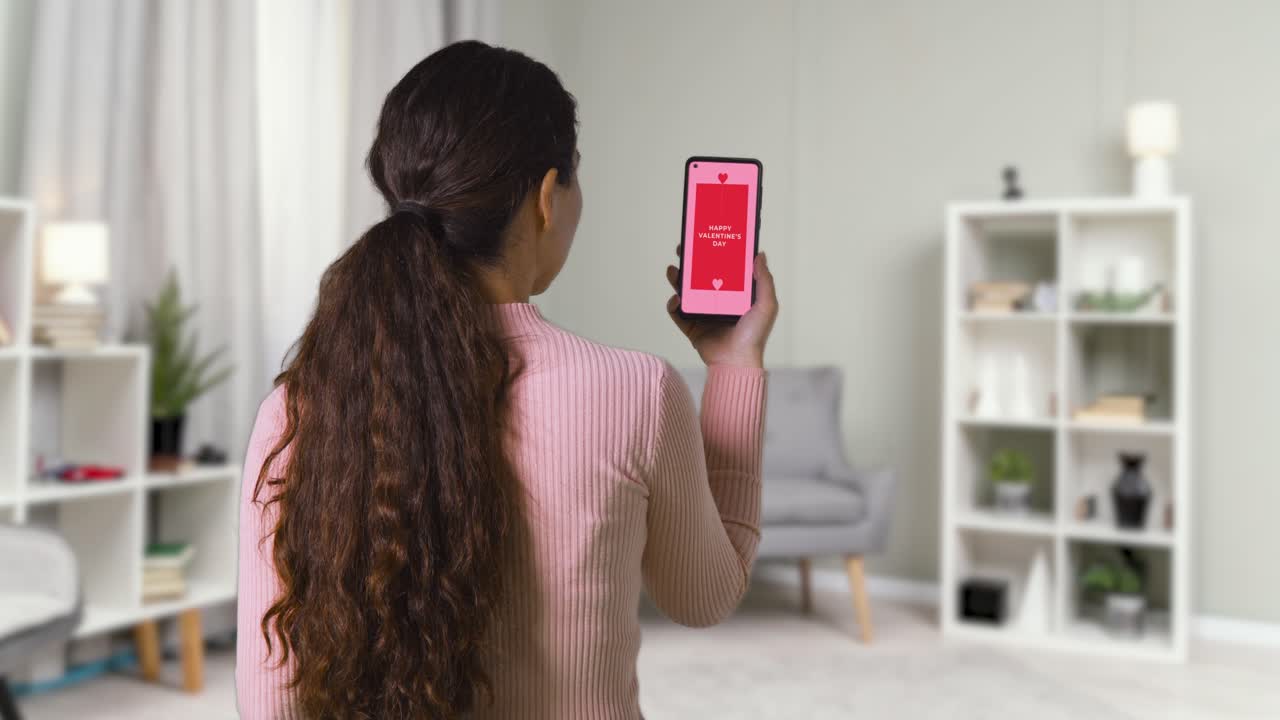 mujer en casa mirando el mensaje de feliz día de san valentín en el teléfono móvil