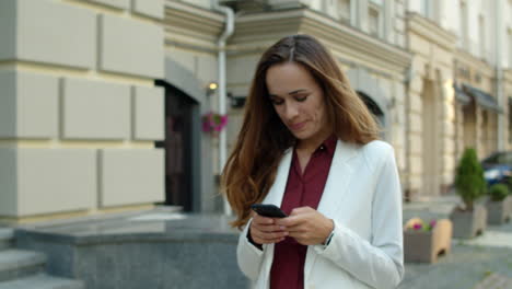 cheerful businesswoman typing message on mobile phone outdoors