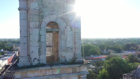 aerial extreme closeup of backlit bell tower with sun glinting along the edge as camera slowly rises above the catedral de san gervasio in valladolid, yucatan, mexico