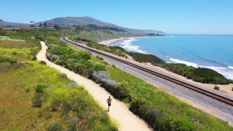 Antena-Sobre-El-Hombre-Corredor-De-Jogging-Ejercicio-A-Lo-Largo-De-Las-Vías-Del-Tren-Del-Sendero-Costero-Y-La-Costa-Del-Pacífico-Cerca-De-Santa-Bárbara-2