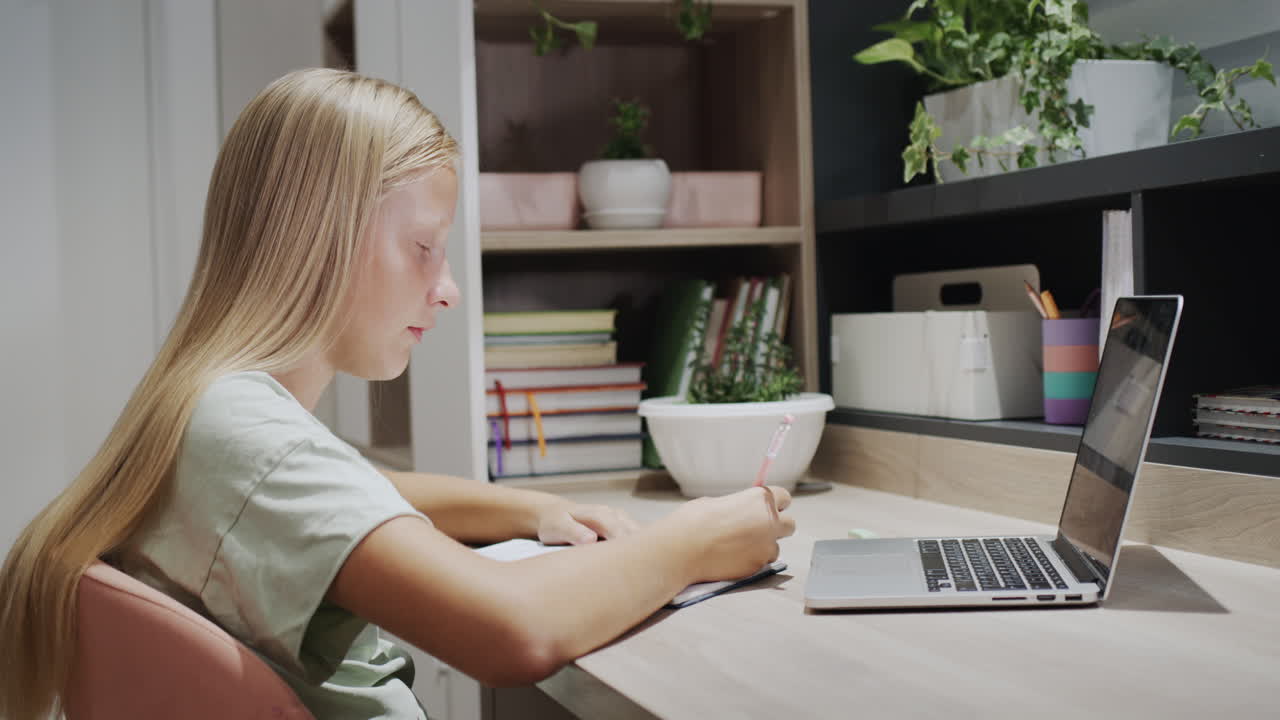 십대 소녀 는 노트북 에 글 을 쓰고, 방 에 있는 노트북 근처 의 테이블 에 앉아 있다. 홈스쿨링 개념
