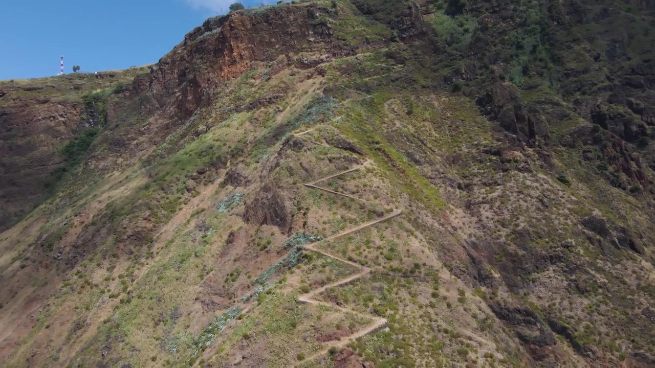 Filmato con drone che si avvicina al Caminho Real dall'alto, rivelando il suo percorso storico scolpito nei ripidi pendii montuosi. Il paesaggio circostante presenta scogliere frastagliate tipiche della costa sud-occidentale di Madeira