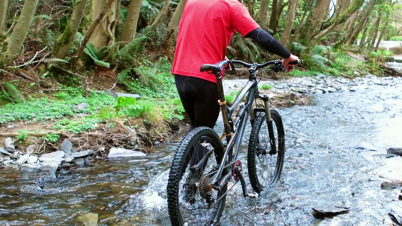 Ciclista in mountain bike che cammina con la bici nel ruscello