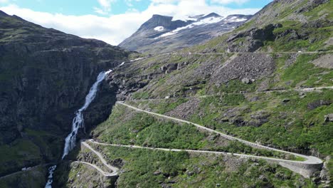 trollstigen mountain road in norway - cars drive touristic route along scenic waterfall and hairpin turns - aerial circling