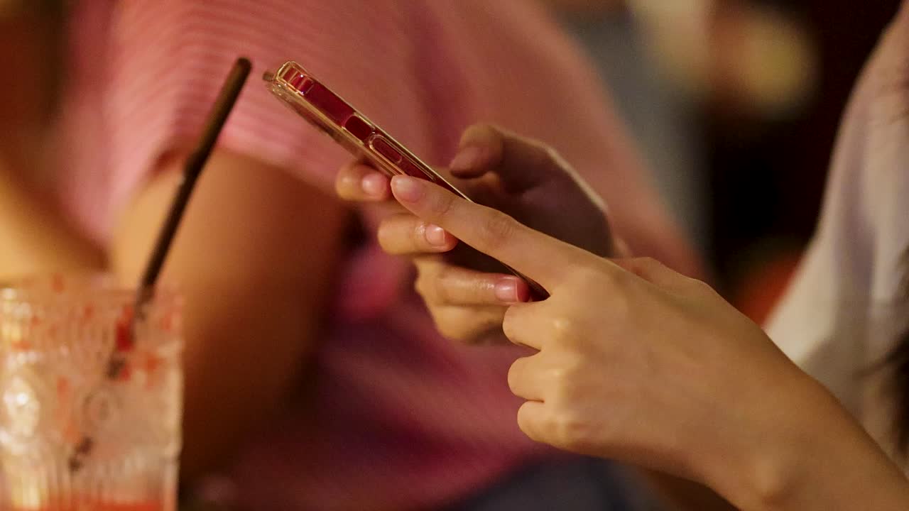 Primo piano di una persona che usa uno smartphone con una mano mentre è seduta a un tavolo di ristorante, illuminazione ambientale calda, profondità di campo ridotta.