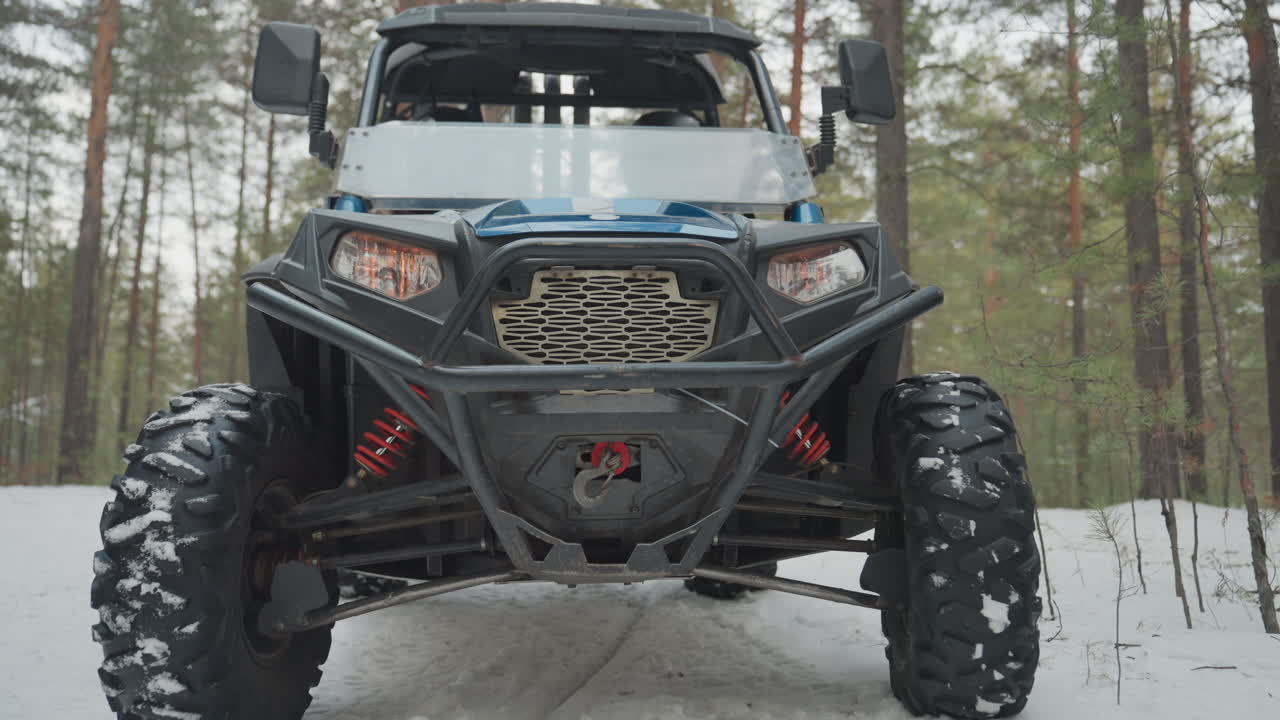 ATV che naviga attraverso una foresta invernale. Fari luminosi illuminano un sentiero boschivo innevato. Potente veicolo fuoristrada con luci brillanti esplora il paesaggio invernale circondato da alberi coperti di neve.