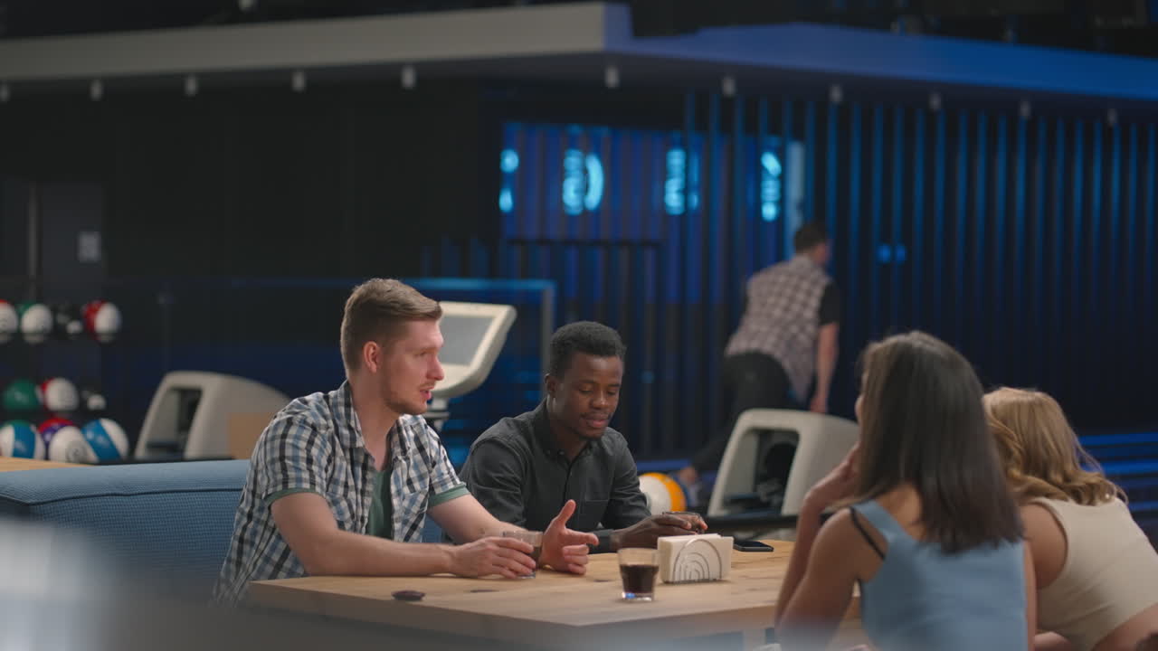 A young man knocks out a strike in a bowling alley and runs up to his friends to rejoice together and give five Together with friends to celebrate the victory. Multi ethnic team of friends