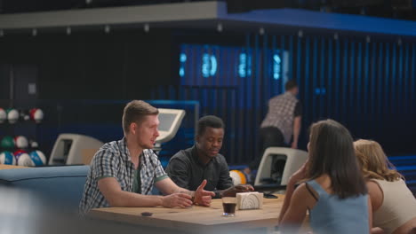 a young man knocks out a strike in a bowling alley and runs up to his friends to rejoice together and give five together with friends to celebrate the victory. multi ethnic team of friends