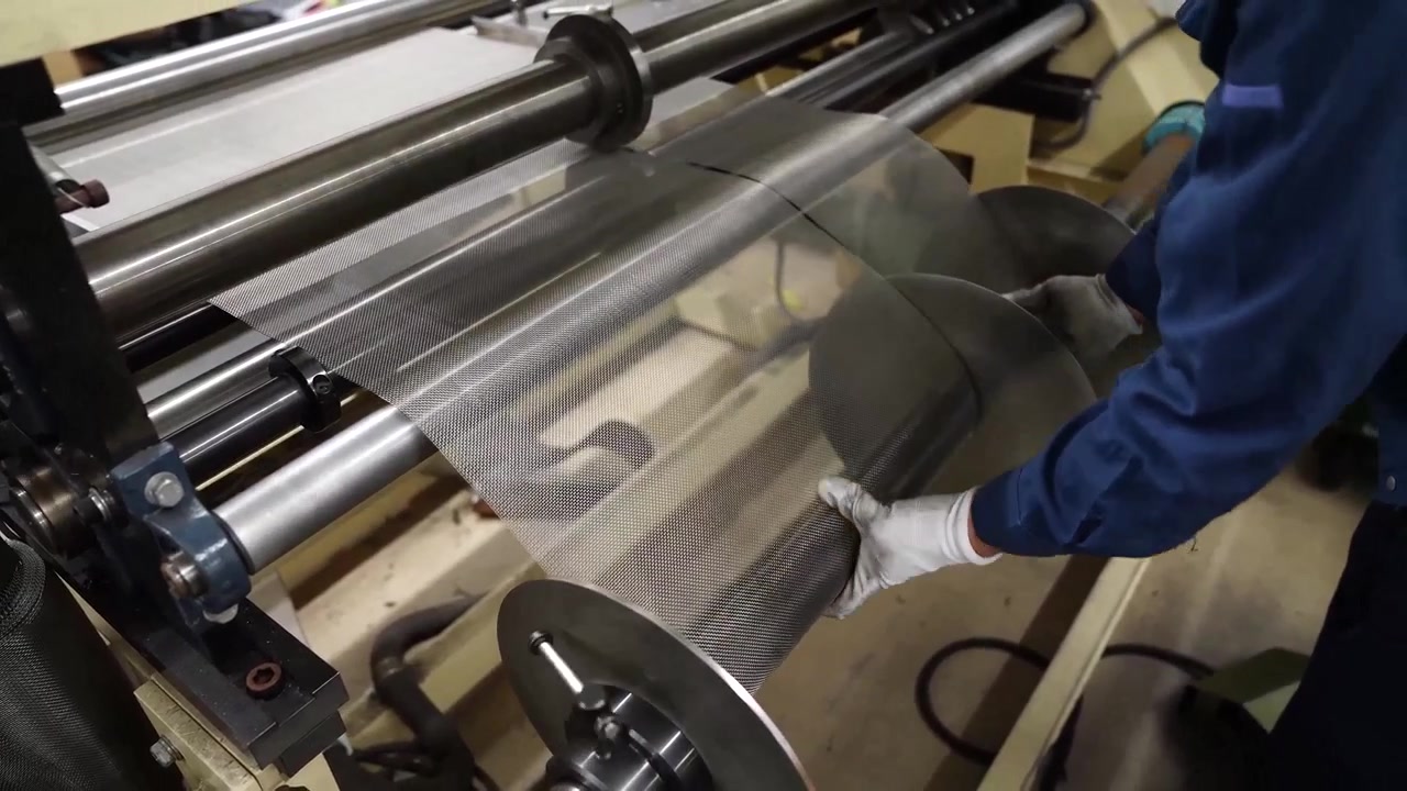 Factory worker feeding perforated steel sheet past spinning blades on an industrial machine
