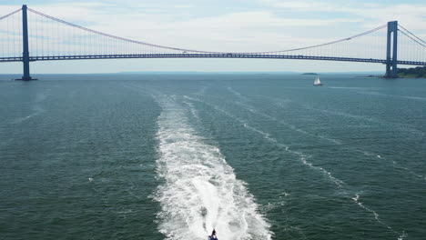 alejándose de 2 motos acuáticas debajo mientras el puente verrazano se revela al fondo de la bahía de brooklyn, nueva york, en una soleada mañana de domingo.