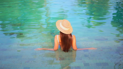 Espalda-De-Mujer-Solitaria-Con-Cabello-Largo-Y-Sombrero-Flexible-Disfrutando-En-El-Agua-De-La-Piscina-En-Un-Caluroso-Día-De-Verano,-Fotograma-Completo