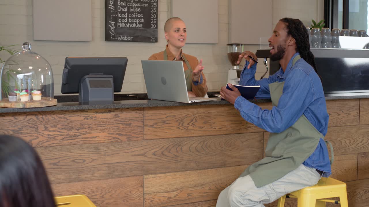 Asian woman walking past speaking into phone causing diverse baristas gesturing at laptop at cafe