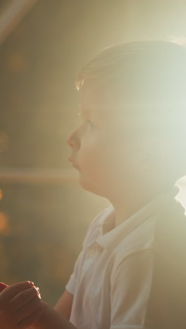 sleepy child stands against lighting near transparent tent wall. dreamy blond kid twirls hands thoughtfully in evening closeup on blurred background slow motion