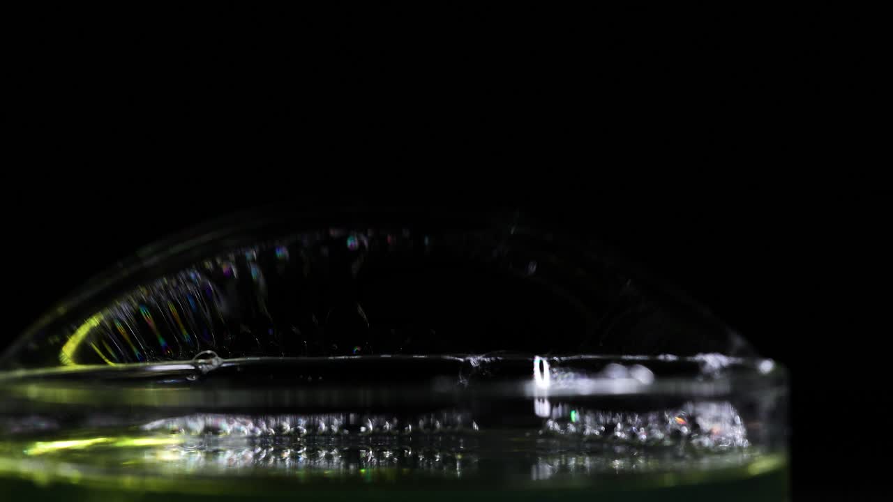 A soap bubble displays vibrant color reflections against a dark background, highlighting its delicate surface tension and iridescence