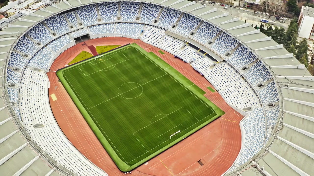 Vista aerea di uno stadio di calcio a Tbilisi, Georgia, che mostra il grande campo verde e le tribune vuote circostanti. La struttura dello stadio è chiaramente visibile dall'alto