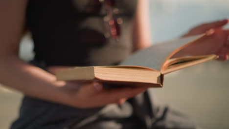 close-up of individual gently holding and flipping the pages of a book as they move to the right due to wind, the individual is slightly blurred same as the background, with a soft sunlight glow