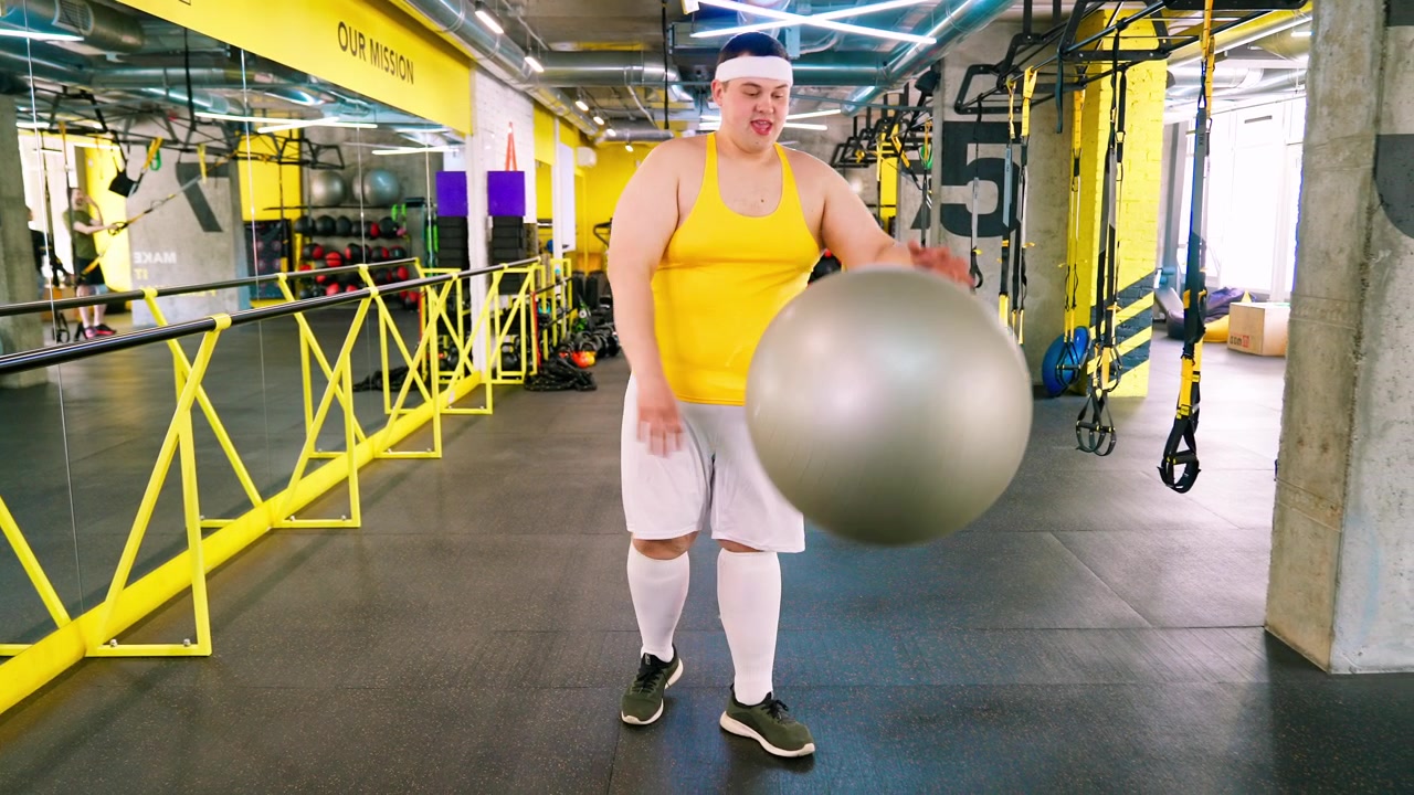 Uomo in sovrappeso che fatica a palleggiare con la palla da ginnastica in palestra