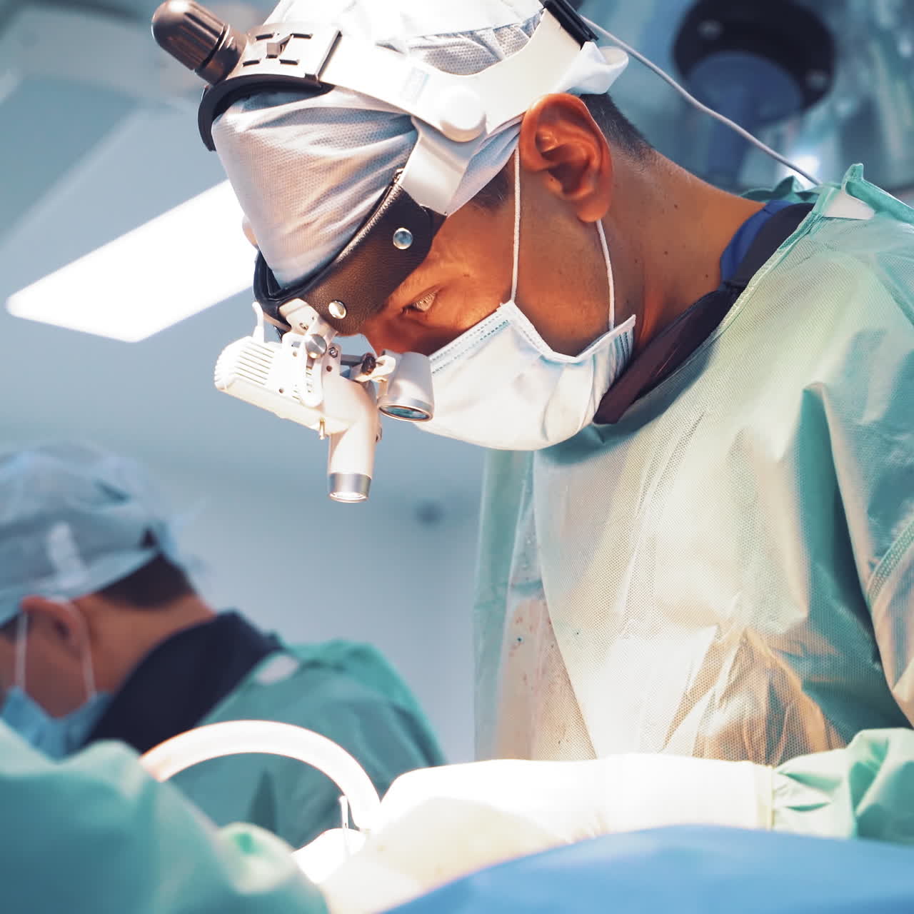 Specialists in medical uniform are doing an operation in hospital. Surgeon with magnifying glass on his head is working with assistants in the operating room. Doctor's concept.
