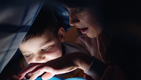 Madre-E-Hijo-Usando-Una-Tableta-Bajo-Una-Manta-Jugando-Juegos-Con-Tecnología-De-Pantalla-Táctil-Niño-Divirtiéndose-Antes-De-Acostarse