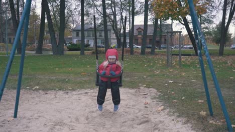 happy girl is swaying on swing in park at autumn day in slow motion