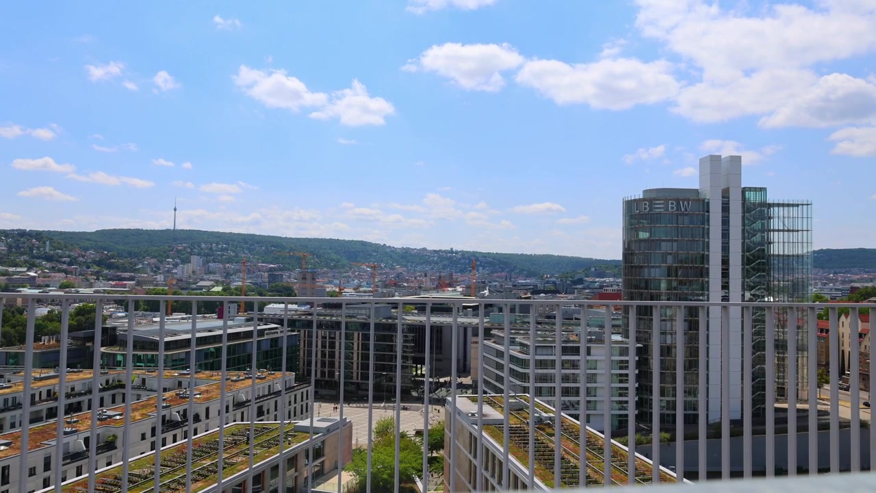 Vista panorâmica da cidade de Stuttgart estendendo-se por telhados e colinas sob um céu claro. Ao longe - a torre de TV.