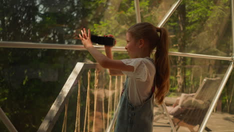 niño con cámara de video en glamping. niña feliz dispara a la naturaleza del bosque en el terreno del hotel ecológico. niño toma fotos del parque en las vacaciones de verano