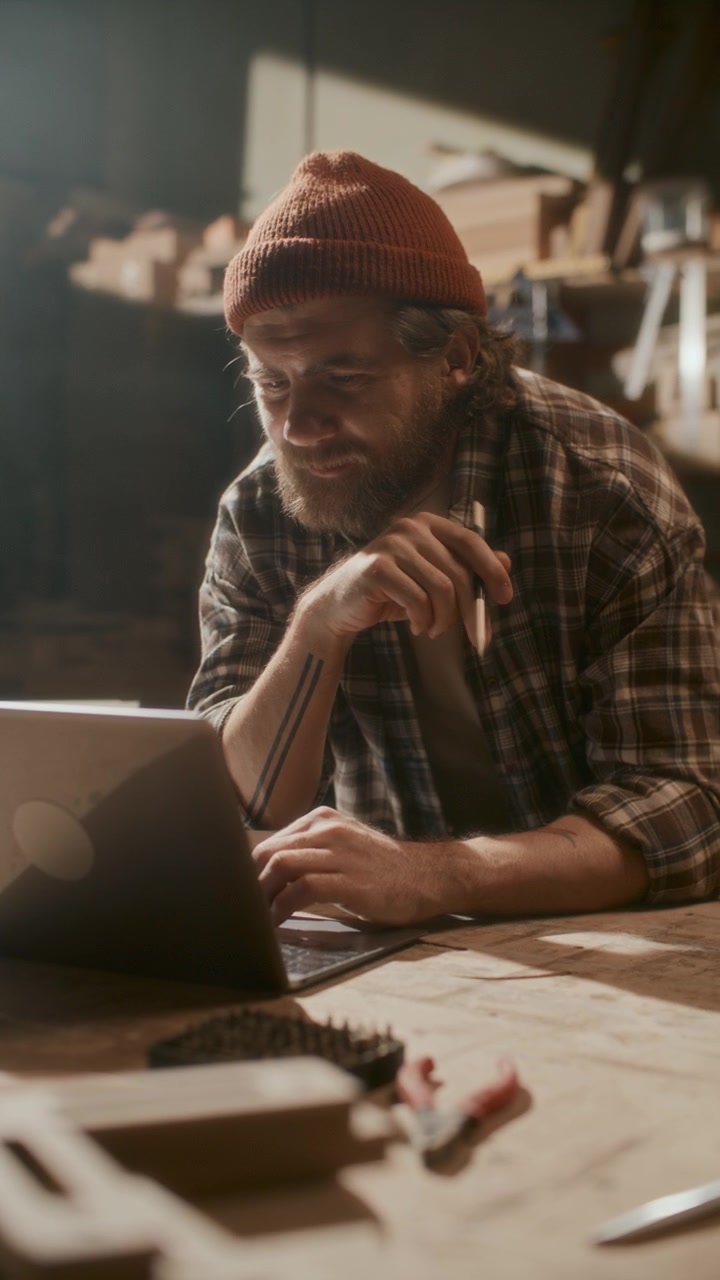 Řemeslník hovořící přes videohovor na notebooku v truhlářské dílně.