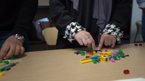 caucasian hands of several people stand in row with colorful interlocking plastic brick piles in front of each person